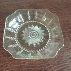 Puede incluir: Un plato de vidrio transparente con un borde festoneado y un diseño decorativo de una estrella con un centro de cuentas.