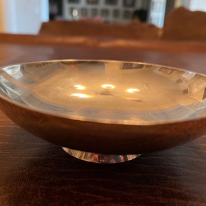 May include: A silver bowl with a rounded base and a smooth, reflective surface. The bowl is sitting on a wooden table.