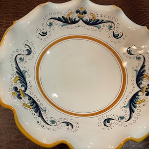 Puede incluir: Un plato de servir de cerámica blanca con un borde festoneado. El plato está decorado con un patrón floral azul y amarillo.
