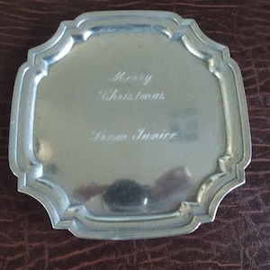 May include: A silver-colored, square-shaped tray with rounded corners and a raised edge. The tray has an inscription that reads "Merry Christmas from Janice".
