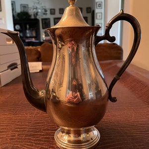 May include: A silver teapot with a shiny, reflective surface. The teapot has a round body, a spout, a handle, and a lid with a knob on top.