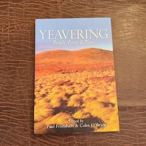 May include: A book titled "Yeavering: People, Power & Place" with a landscape image on the cover. The cover features a blue sky, a brown hill, and golden grass. The book is edited by Paul Froodsham & Colm O'Brien.