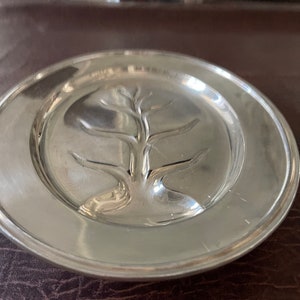 May include: A silver plate with a raised design of a tree in the center.