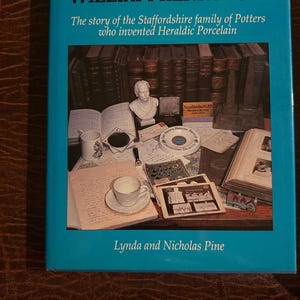 May include: A hardcover book titled William Henry Goss: The story of the Staffordshire family of Potters who invented Heraldic Porcelain by Lynda and Nicholas Pine. The cover features a collage of antique books, a bust, and porcelain items.