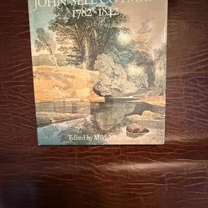 Puede incluir: Un libro titulado "JOHN SELL COTMAN 1782-1842" con una pintura de paisaje en la portada. La ilustración muestra árboles, agua y reflejos. El libro está editado por Miklos Rajnai.