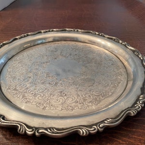 May include: A silver serving tray with a decorative, swirling pattern. The tray has a scalloped edge.
