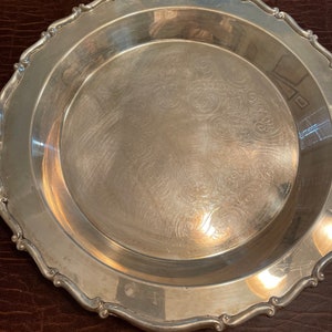 May include: A silver serving tray with a scalloped edge and an ornate design. The tray is made of metal and has a shiny finish.
