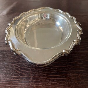 May include: A silver oval-shaped serving dish with a scalloped edge. The dish is made of polished metal and has a reflective surface.
