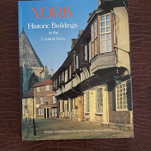 Könnte beinhalten: Ein Softcover-Buch mit dem Titel YORK Historic Buildings in the Central Area von der Royal Commission on Historical Monuments. Das Cover zeigt ein Foto von historischen Fachwerkhäusern und einem Kathedralenturm vor blauem Himmel.