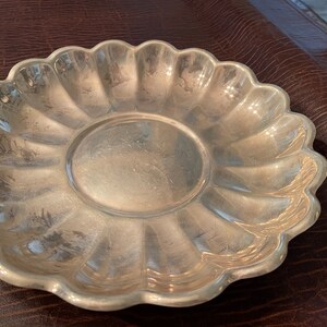 May include: A silver serving dish with a scalloped edge and a fluted design. The dish is made of metal and has a shiny finish.