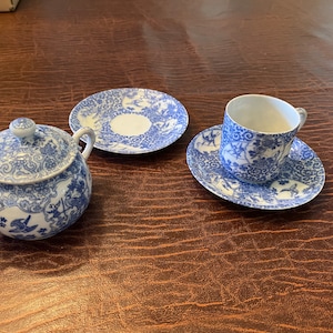 Op de afbeelding: Een blauw en wit porseleinen theeservies met een suikerpot, roomkan, kopje en schotel. Het servies heeft een bloemenpatroon met blauwe bloemen en bladeren op een witte achtergrond.