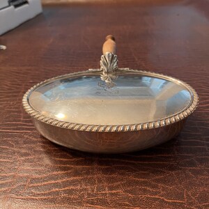 May include: A silver oval-shaped dish with a wooden handle. The dish has a decorative rope-like border around the edge.