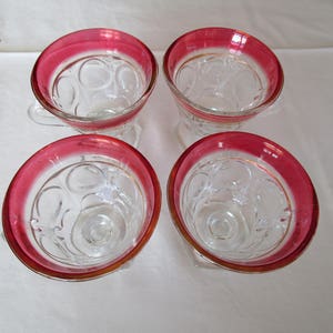 Puede incluir: Cuatro vasos de vidrio transparente con borde rojo y un patrón de pequeños círculos. Los vasos están sobre un mantel blanco.