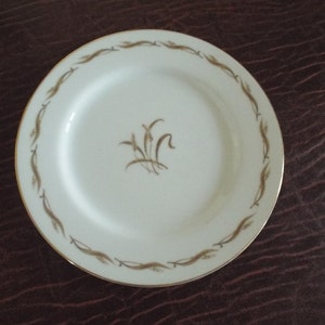 May include: A white ceramic plate with a gold rim and a brown floral design in the center. The plate is on a brown surface.