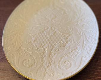 Könnte beinhalten: Weiße ovale Servierplatte mit einem erhabenen, geprägten Blumendesign und einem goldenen Rand.