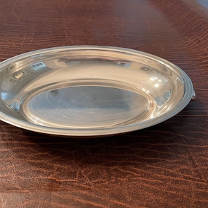 May include: A silver oval serving dish with two handles. The dish is polished and reflects light.