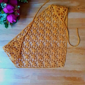 May include: A triangular mustard yellow crochet bandana featuring an intricate openwork floral pattern. The accessory is crafted with thin yarn and includes long, slender ties at the top corners for securing the piece around the head or neck.