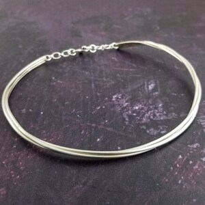 May include: A silver choker necklace with a simple design. The necklace is made of three strands of silver wire that are twisted together.