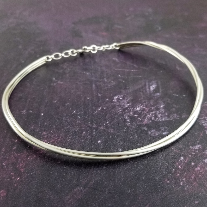 May include: A silver choker necklace with a simple design. The necklace is made of three strands of silver wire that are twisted together.