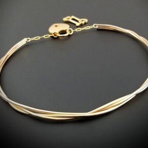 May include: A gold-toned choker necklace with a heart-shaped padlock and a key charm. The necklace is made of multiple strands of twisted wire.