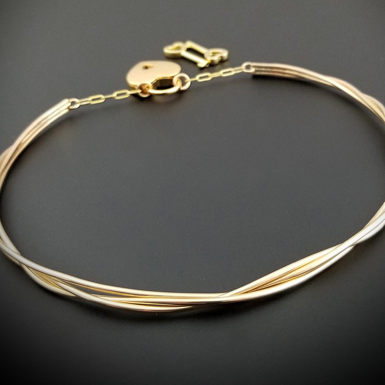 May include: A gold-toned choker necklace with a heart-shaped padlock and a key charm. The necklace is made of multiple strands of twisted wire.