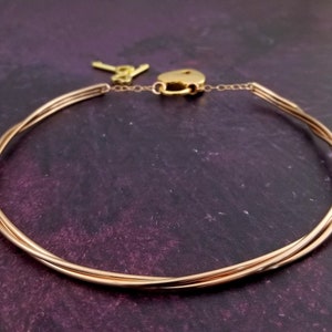 May include: A gold-toned choker necklace with a lock and key. The necklace is made of multiple strands of wire that are twisted together.