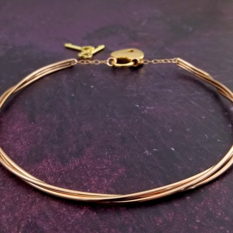 May include: A gold-toned choker necklace with a lock and key. The necklace is made of multiple strands of wire that are twisted together.