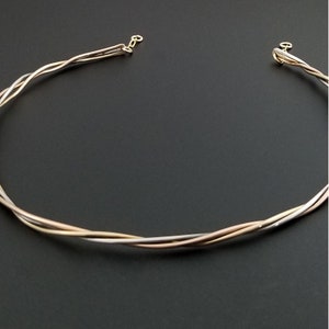 May include: A gold, silver, and rose gold twisted wire necklace. The necklace is made of three strands of wire that are twisted together.
