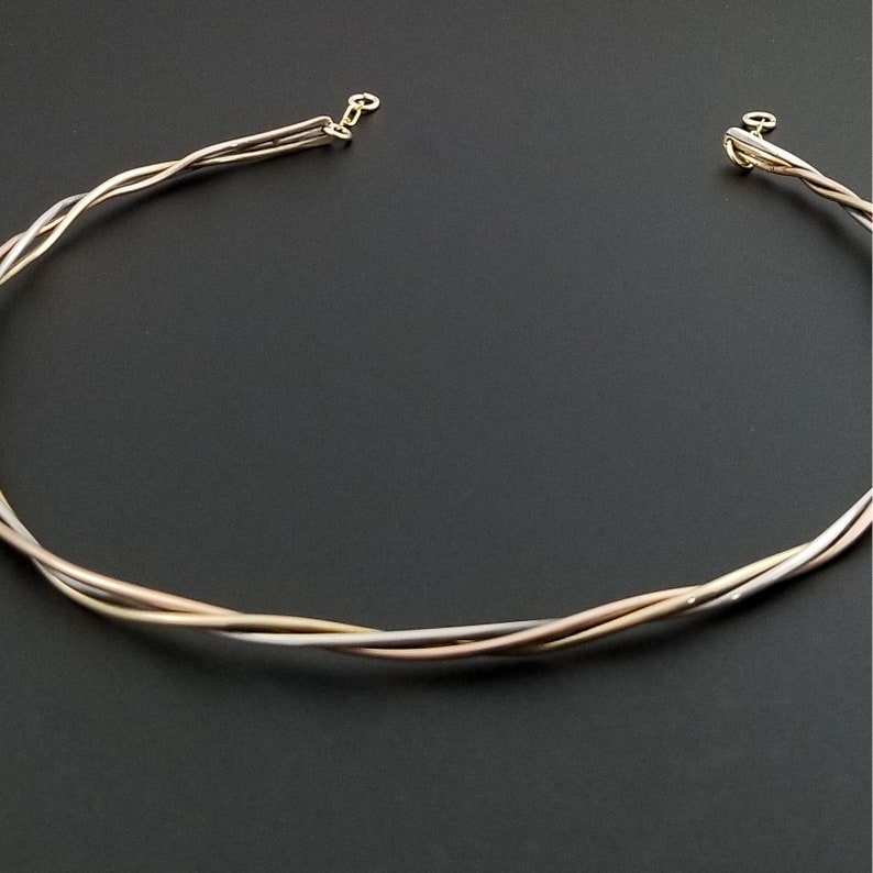 May include: A gold, silver, and rose gold twisted wire necklace. The necklace is made of three strands of wire that are twisted together.