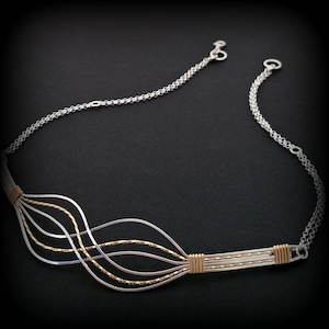 Puede incluir: Un collar de plata y oro con un diseño ondulado. El collar está hecho de varios hilos de alambre que están entrelazados.