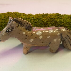 Puede incluir: Una peque&ntilde;a figurita de caballo de cer&aacute;mica con pintura moteada marr&oacute;n y blanca. El caballo tiene una cola y una crin largas.