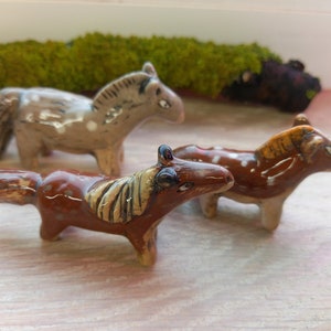 Puede incluir: Tres figuritas de caballos de cer&aacute;mica, una marr&oacute;n con manchas blancas, una marr&oacute;n con manchas blancas y una crin marr&oacute;n claro, y una marr&oacute;n claro con manchas blancas.