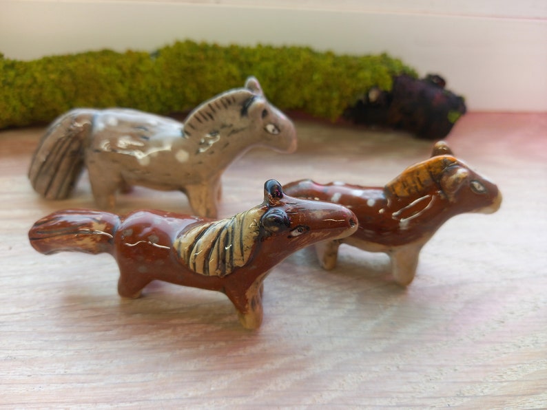 Puede incluir: Tres figuritas de caballos de cer&aacute;mica, una marr&oacute;n con manchas blancas, una marr&oacute;n con manchas blancas y una crin marr&oacute;n claro, y una marr&oacute;n claro con manchas blancas.