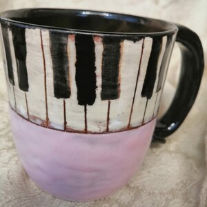May include: A ceramic coffee mug with a black and white piano key design and a pink bottom.