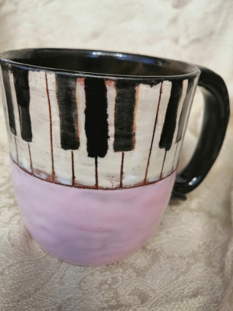 May include: A ceramic coffee mug with a black and white piano key design and a pink bottom.