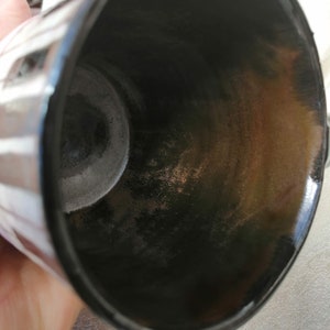 May include: Close-up view of the inside of a black ceramic mug with a white stripe pattern. The interior of the mug shows signs of wear and discoloration.