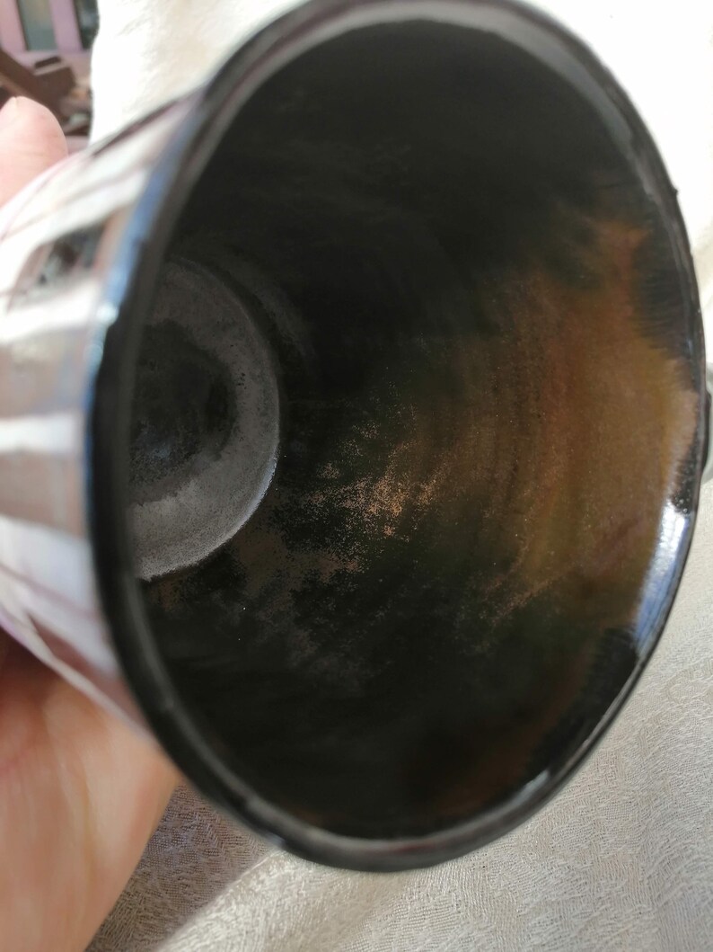 May include: Close-up view of the inside of a black ceramic mug with a white stripe pattern. The interior of the mug shows signs of wear and discoloration.