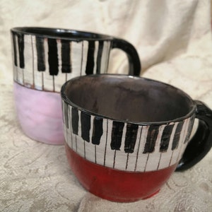 May include: Two ceramic mugs with black and white piano key designs. One mug has a pink base and the other has a red base.
