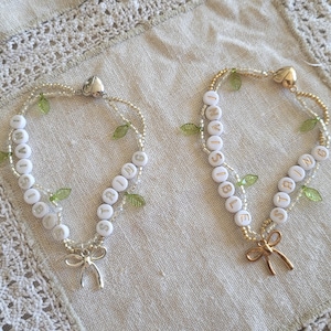 May include: Two white beaded bracelets with green leaf charms. One bracelet says "My Sister" and the other says "Is Amazing".