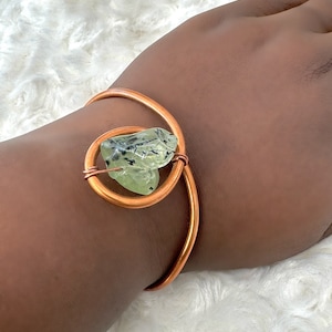 May include: A copper wire bracelet with a green and black stone wrapped in the wire.
