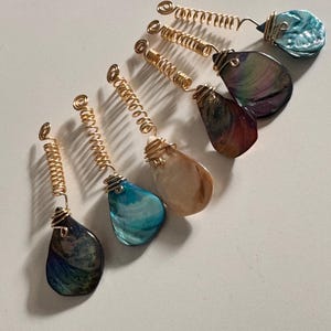 May include: Six gold hair coils with iridescent shell charms. The shells are in shades of blue, green, brown, and white.