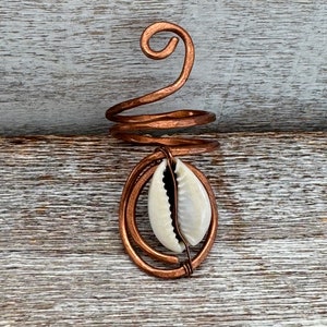 May include: A copper wire ring with a white cowrie shell hanging from it. The ring is coiled and has a spiral design.