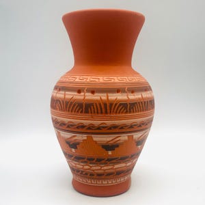 May include: Terracotta vase with a wide base and flared rim. The vase features intricate, hand-carved designs in shades of brown and cream, including geometric patterns and stylized landscape elements. The vase is approximately 10 inches tall.