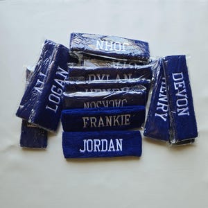 Puede incluir: Un conjunto de cintas para la cabeza de color azul marino con nombres bordados en blanco. Los nombres incluyen Logan, John, Dylan, Jackson, Frankie, Jordan, Henry y Devon. Las cintas est&aacute;n envueltas individualmente en pl&aacute;stico transparente.