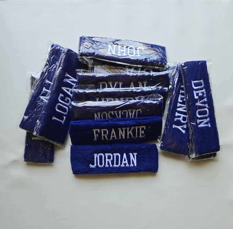 Puede incluir: Un conjunto de cintas para la cabeza de color azul marino con nombres bordados en blanco. Los nombres incluyen Logan, John, Dylan, Jackson, Frankie, Jordan, Henry y Devon. Las cintas est&aacute;n envueltas individualmente en pl&aacute;stico transparente.