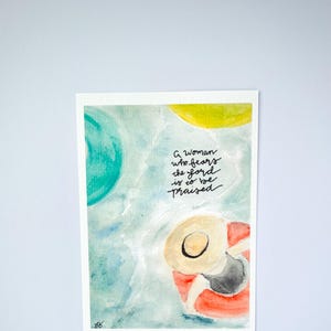 May include: A watercolor painting of a woman wearing a hat and sitting in a red and white life preserver. The background is a blue and green watercolor wash. The text "A woman who fears the Lord is to be praised" is written in black ink.