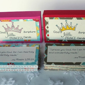 Puede incluir: Dos juegos de peque&ntilde;as cajas coloridas con tarjetas de escrituras en su interior. Las cajas est&aacute;n decoradas con coronas y el texto "God's little PRINCESS Cards" y "God's little PRINCE Cards". Las tarjetas tienen vers&iacute;culos de la escritura impresos en ellas.