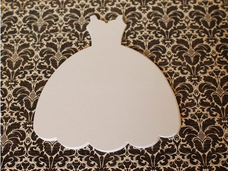 Pu&ograve; includere: Taglio di carta bianco a forma di abito da sposa. Il taglio &egrave; su uno sfondo marrone a motivi.