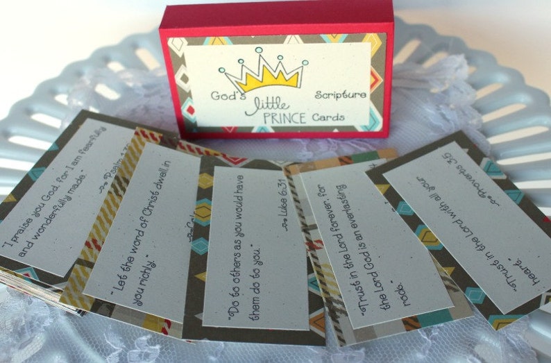 Puede incluir: Un juego de peque&ntilde;as tarjetas con citas b&iacute;blicas inspiradoras impresas en ellas. Las tarjetas est&aacute;n decoradas con un patr&oacute;n geom&eacute;trico en tonos marrones, azules y amarillos. Las tarjetas est&aacute;n empaquetadas en una peque&ntilde;a caja con una tapa roja y un patr&oacute;n geom&eacute;trico en la parte delantera. La caja tiene las palabras "God's Little Prince Cards" impresas en ella.