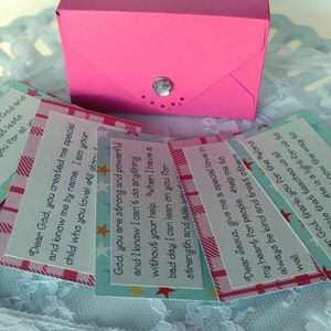 Puede incluir: Una pila de peque&ntilde;as tarjetas coloridas con mensajes inspiradores sobre Dios y Jes&uacute;s. Las tarjetas est&aacute;n decoradas con estrellas y patrones de cuadros. Las tarjetas est&aacute;n en una caja rosa.